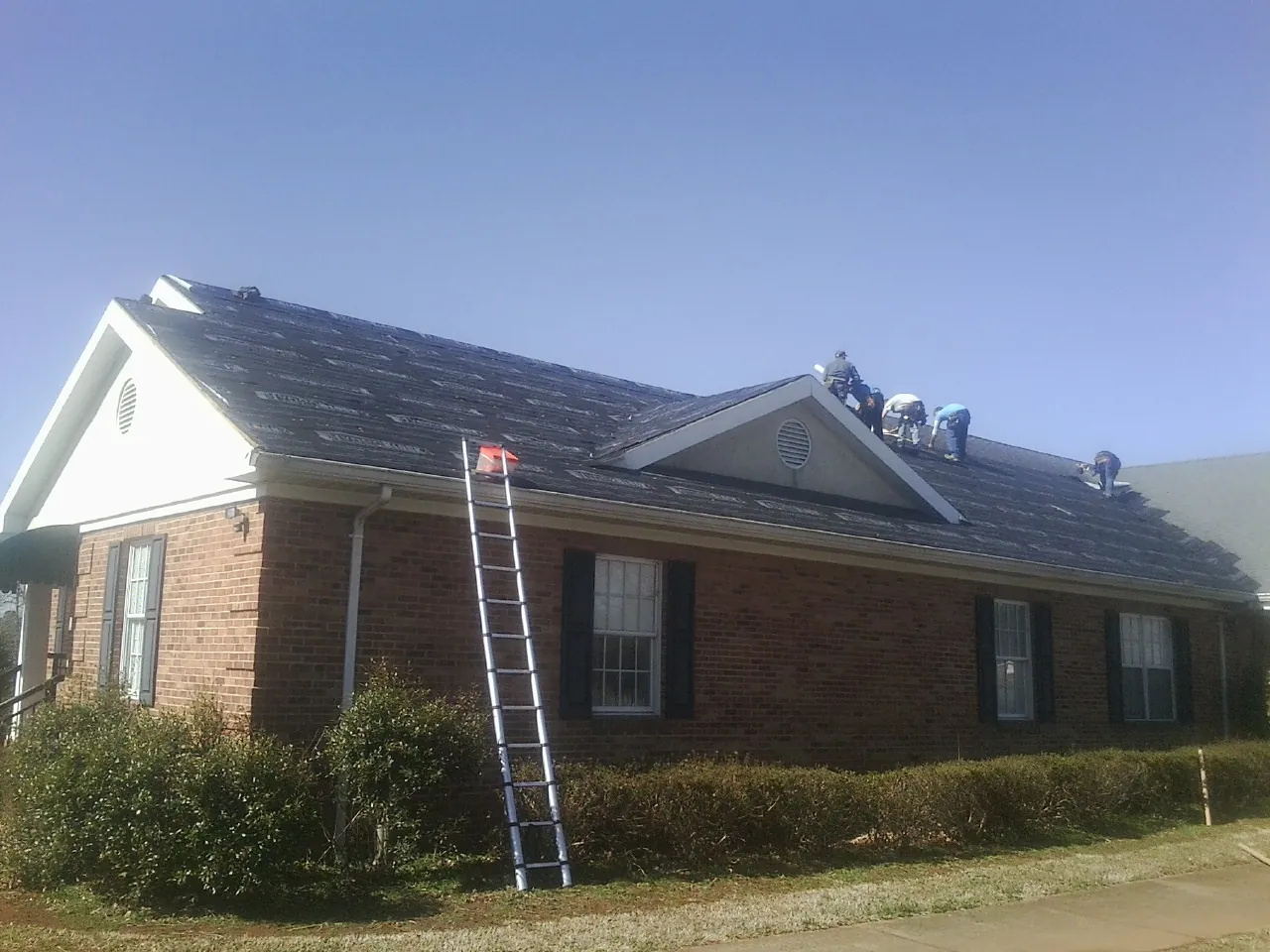 Crew tearing shingles off a brick ranch roof with a ladder set — Metal Roof Repair work by our crew in Laurelville