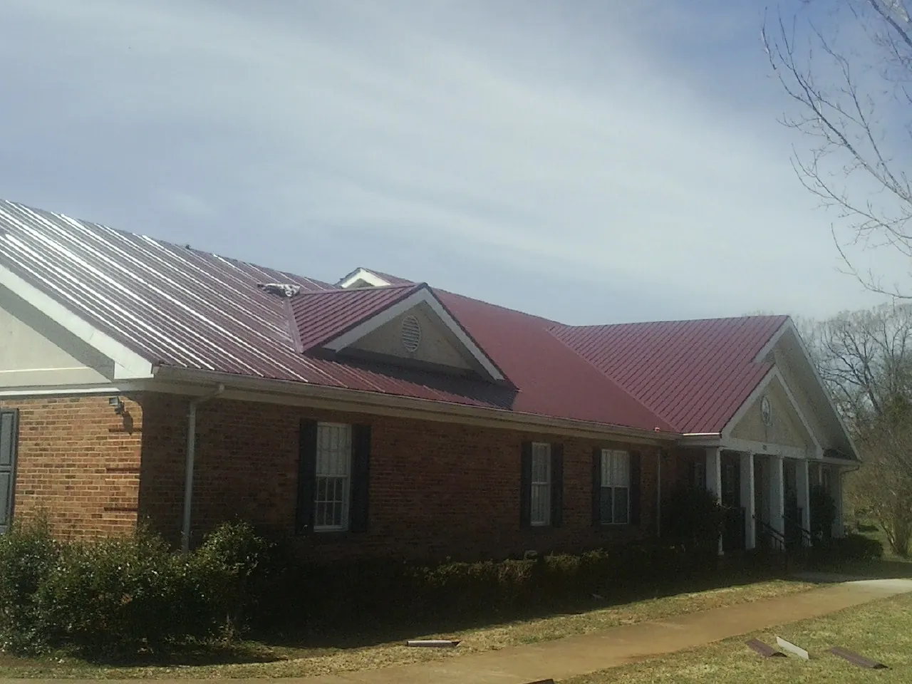 Red metal roof with gabled entries on a long brick building, from a Hail Damage Roof Repair job in Laurelville