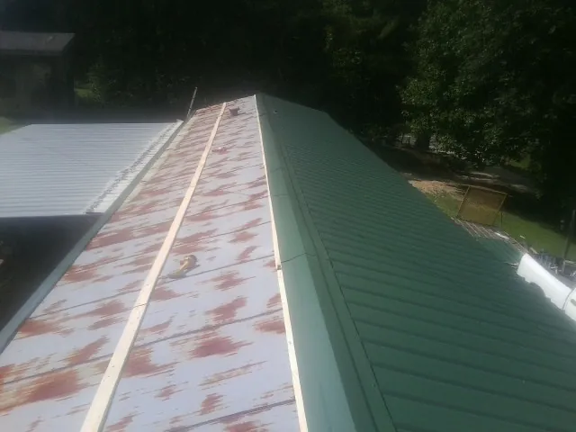 Old rusted panels beside newly installed green metal roofing — Wind Damage Roof Repair by Roofing Brothers in Laurelville