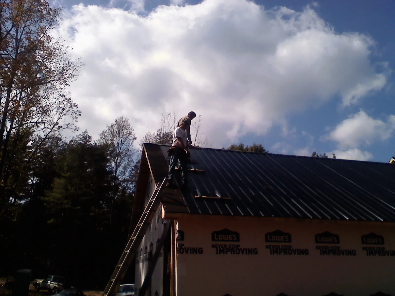 Roofer fastening dark metal panels high against a cloudy sky, from a Roof Inspection job in Laurelville