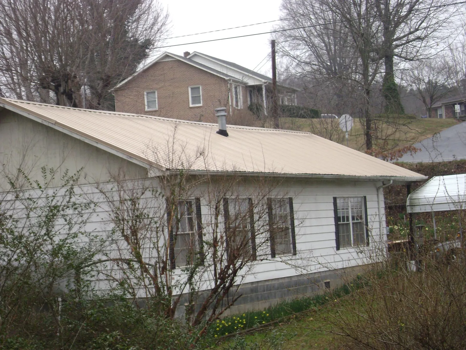 Tan metal roof on a white sided house set into a hillside — Commercial Roofing by Roofing Brothers in Laurelville