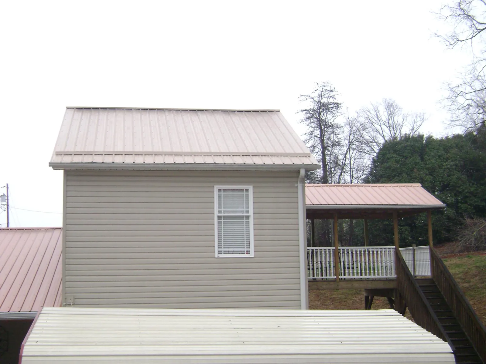 Tan metal roofs on a two story addition and attached porch, from a Roof Replacement job in Laurelville